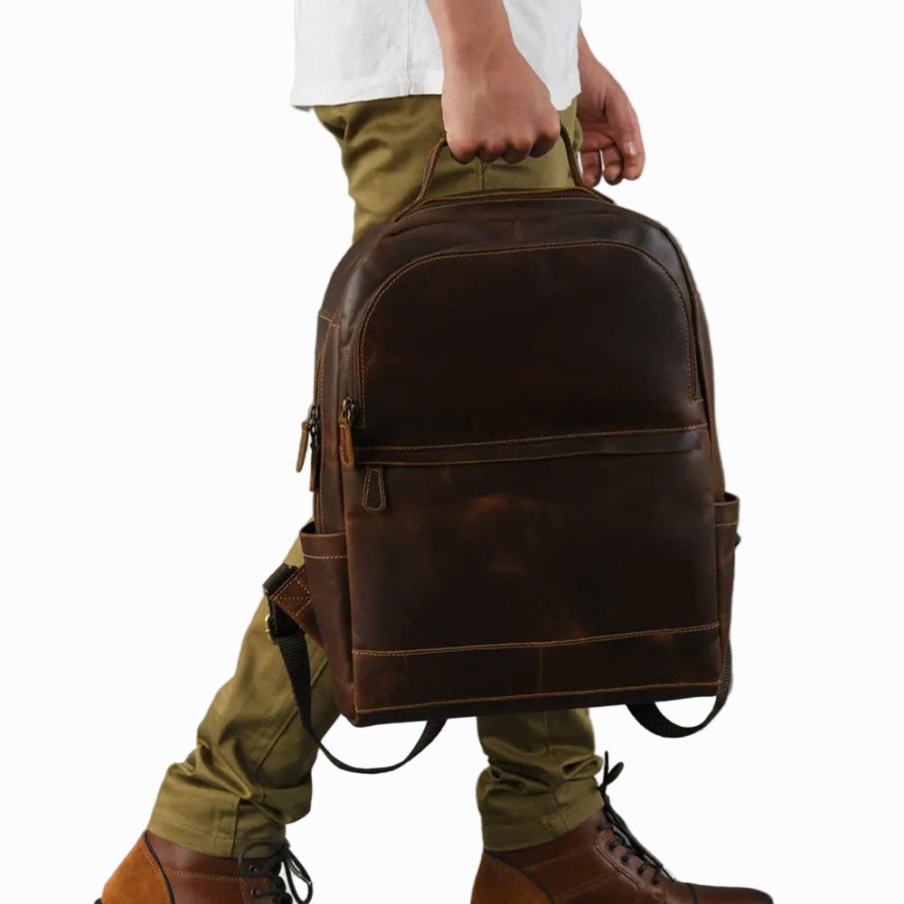 Person holding a brown vintage distressed unisex backpack against a gray background