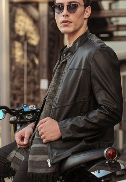 A man wearing a black leather jacket and sunglasses is standing next to a motorcycle.