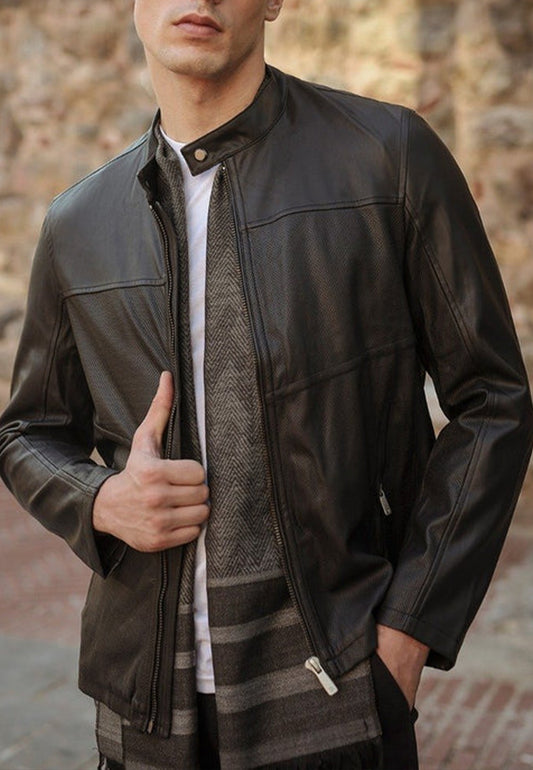 Man wearing a black leather jacket with a textured scarf against a stone wall background
