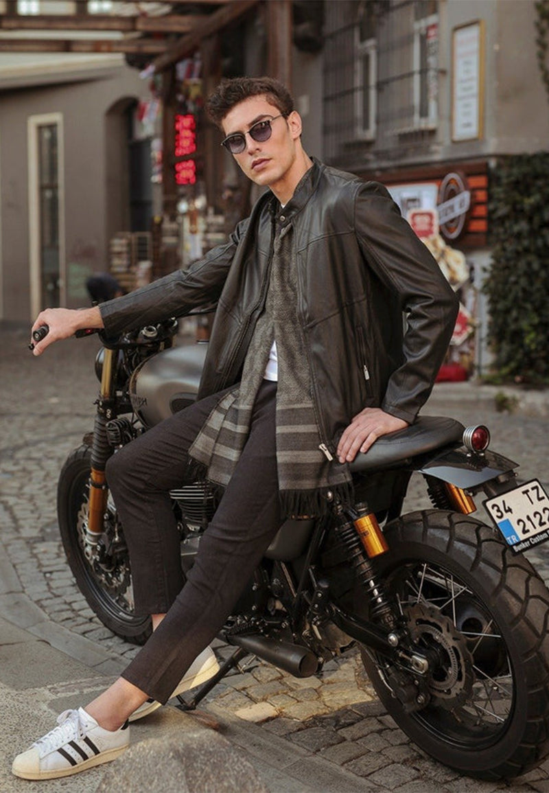 Man sitting on a motorcycle wearing sunglasses and a genuine sheepskin leather jacket in an urban setting.