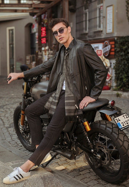 Man sitting on a motorcycle wearing sunglasses and a genuine sheepskin leather jacket in an urban setting.