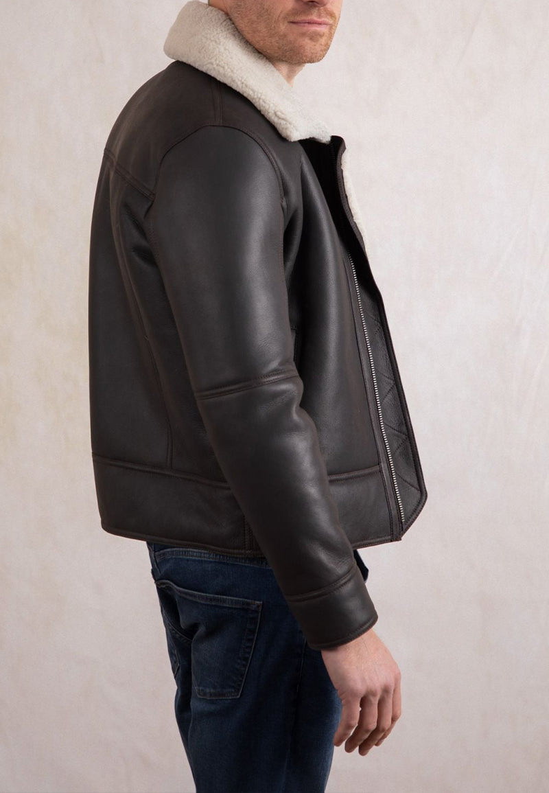Man wearing a dark brown shearling leather jacket with white fur lining on a neutral background