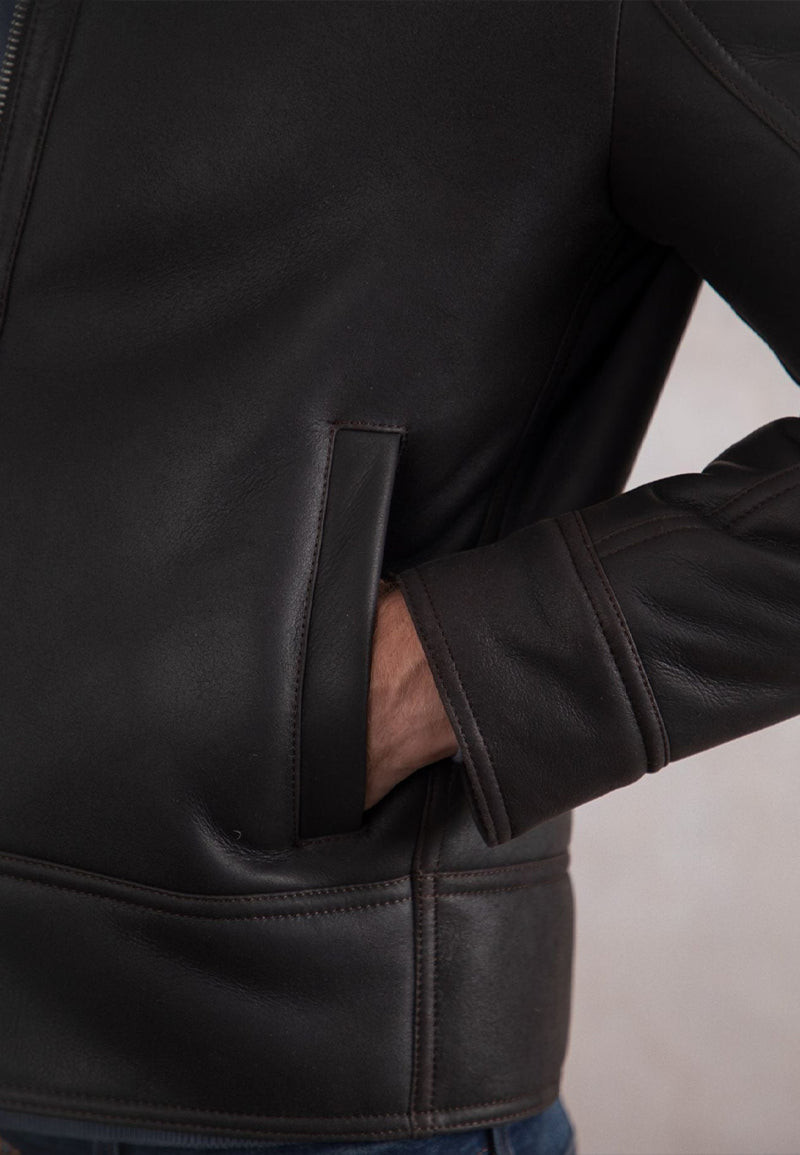 Close-up of a person wearing a brown genuine leather shearling jacket with a neutral background