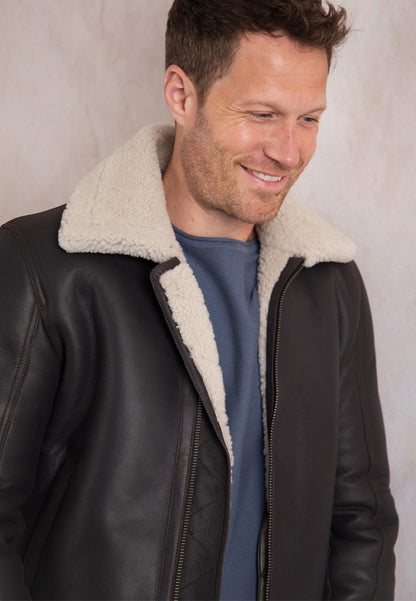 Man wearing a brown shearling leather jacket with white fur lining against a neutral background