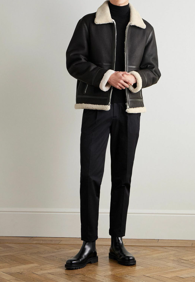 Person wearing a black shearling leather jacket with white fur trim on a plain background 