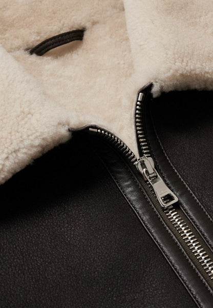 Close-up of a black leather vintage shearling jacket with a zipper and beige shearling lining.