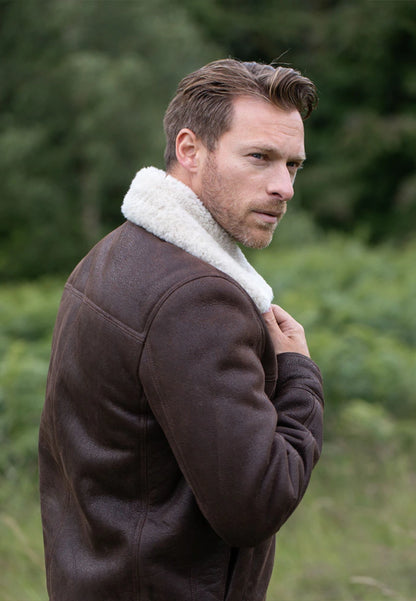 Man wearing a brown shearling jacket in a forest setting