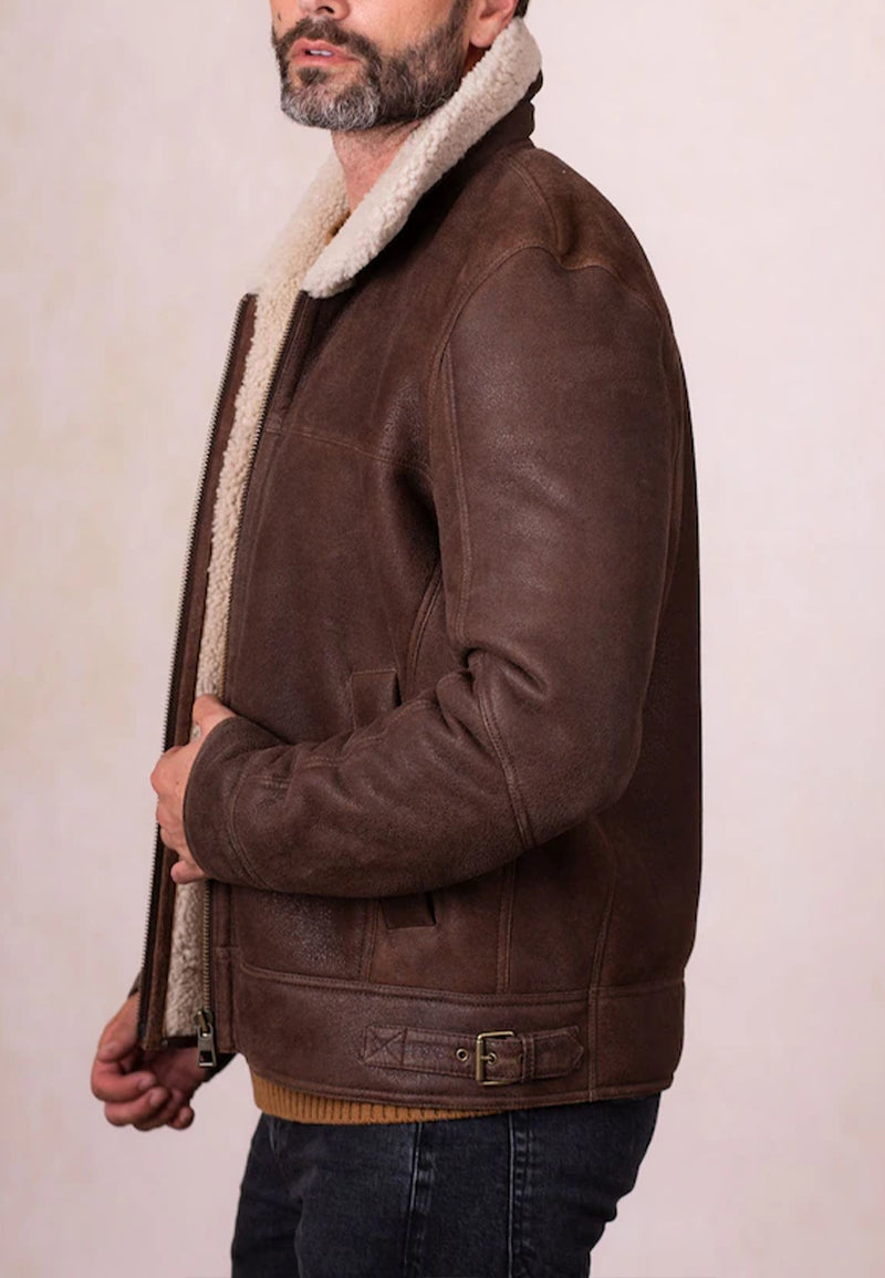 Man wearing a brown shearling aviator jacket with white fur lining on a plain background