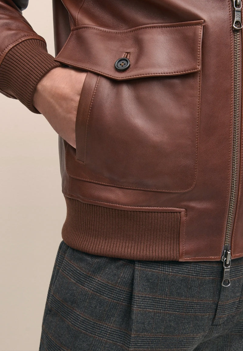 Close-up of a brown leather jacket with a pocket and zipper on a neutral background
