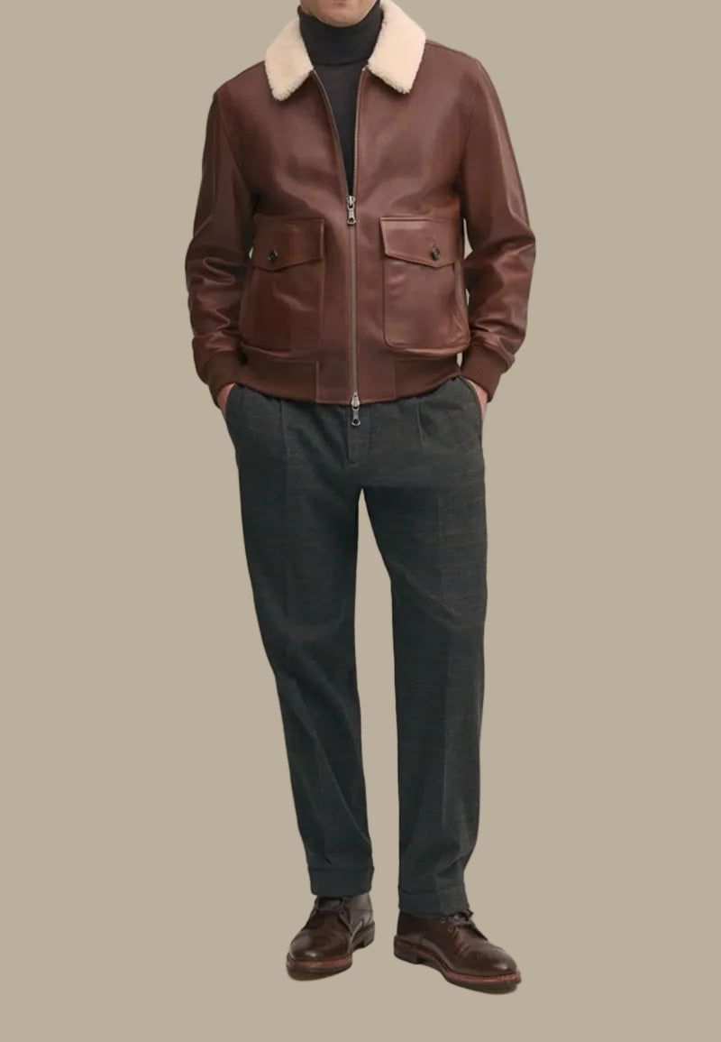 Person wearing a brown sheepskin leather bomber jacket with a white fur collar, dark pants, and brown shoes against a neutral background.