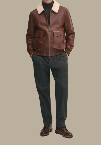 Person wearing a brown sheepskin leather bomber jacket with a white fur collar, dark pants, and brown shoes against a neutral background.