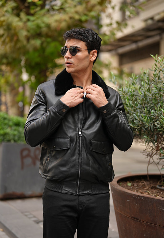 A man wearing a black leather jshearling coat acket and sunglasses outdoors.
