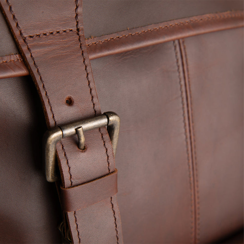 Close-up of a brown full-grain sheepskin leather bag with a strap and buckle.