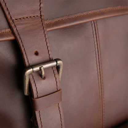 Close-up of a brown full-grain sheepskin leather bag with a strap and buckle.