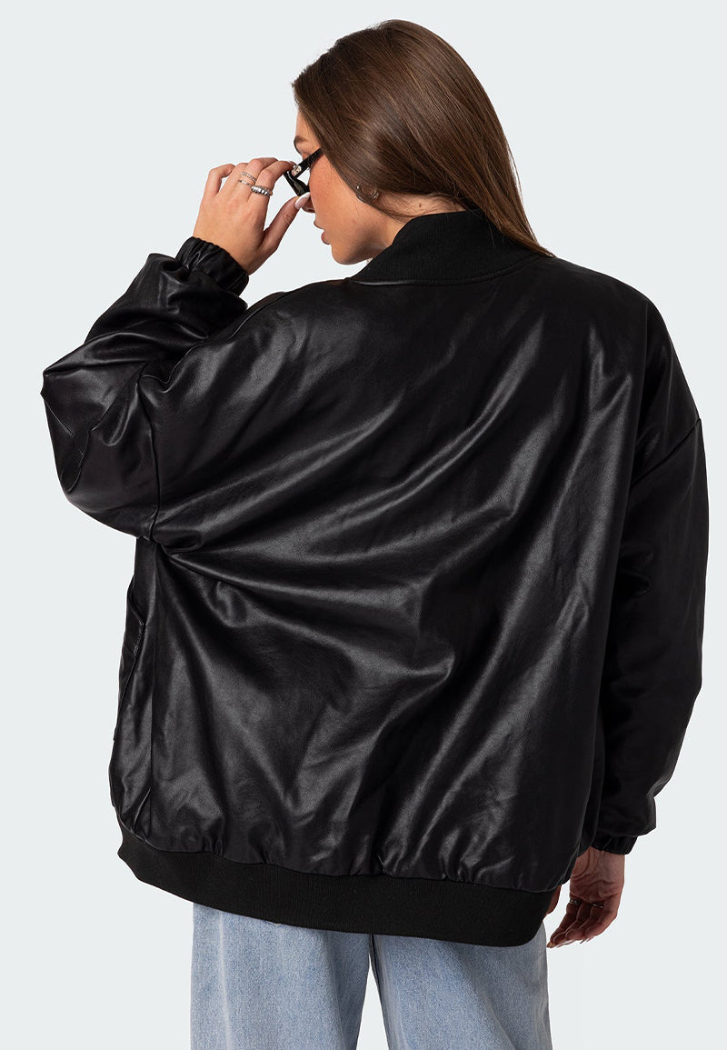 Rear view of a model wearing a black oversized leather bomber jacket with black sunglasses