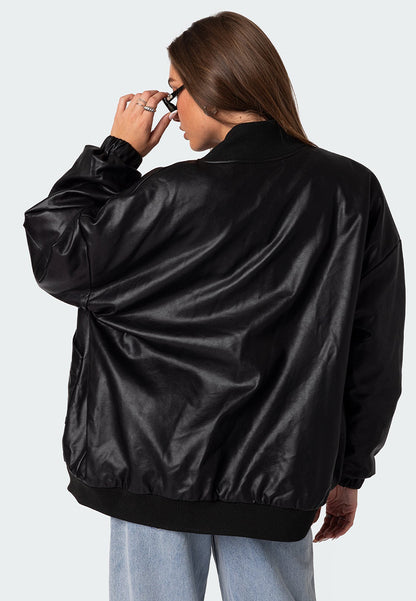 Rear view of a model wearing a black oversized leather bomber jacket with black sunglasses