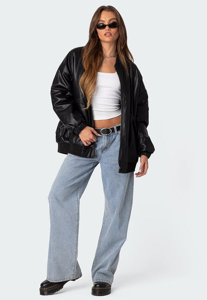 front view of a model wearing a black oversized leather bomber jacket with black sunglasses